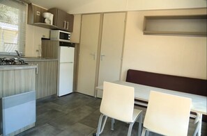 Uma cozinha compacta com fogão a gás, micro-ondas e frigorífico, uma mesa de jantar com duas cadeiras e um banco.