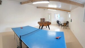 Une pièce équipée d’une table de ping-pong, d’un baby-foot et de deux chaises.