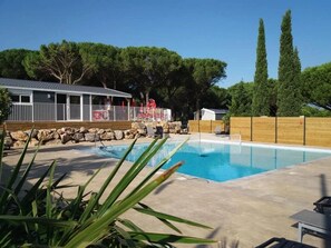 Une piscine avec une terrasse en bois, un espace clôturé et un bâtiment doté d’un patio couvert.