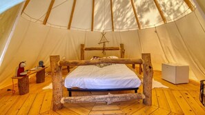 A tent with a bed, a small table, and a white object on the floor.