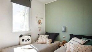 Ein Schlafzimmer mit zwei Betten, einem Fenster mit Jalousie, einer Wanddekoration und einem kleinen Tisch mit Lampe.