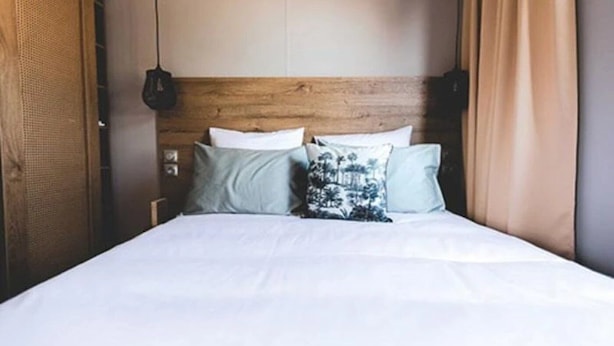 A bed with a wooden headboard, white bedding, and two pillows with a floral pattern.