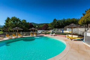Une piscine entourée d’une clôture et d’arbres, avec des chaises longues et des parasols à proximité.