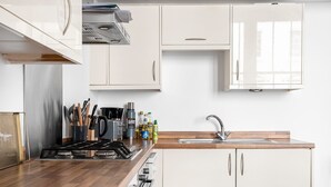 Une cuisine moderne avec des armoires blanches, un plan de travail en bois, une cuisinière encastrée et un évier en acier inoxydable.