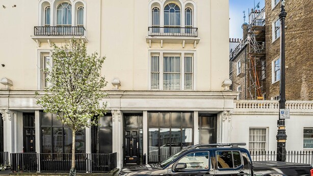 Un immeuble de deux étages avec une façade blanche, de grandes fenêtres et une voiture noire garée devant.