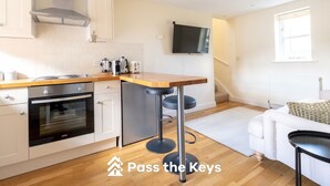 A modern kitchen with white cabinets, a wooden countertop, and a built-in oven. There is a bar stool and a TV mounted on the wall. - Cosy loft apartment near Oxford - Pass the Keys (Abingdon)