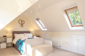 A bedroom with a sloped ceiling, a bed, a nightstand, a lamp, a radiator, and a wardrobe.