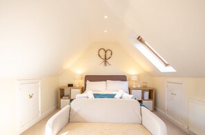 A bedroom with a bed, bedside tables, a nightstand, a wall decoration, and a skylight.