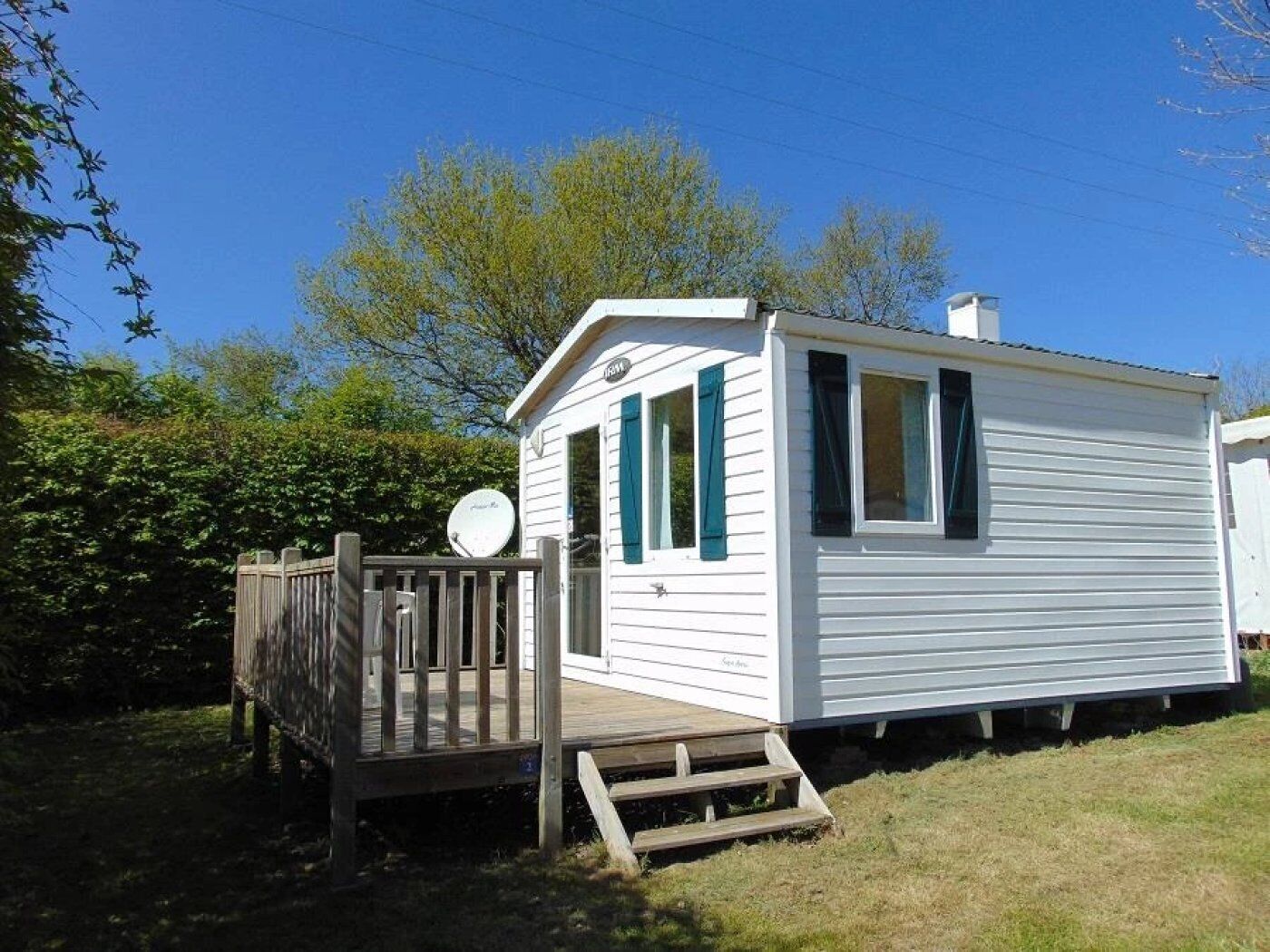 A small, single-story mobile home with a deck and a satellite dish.