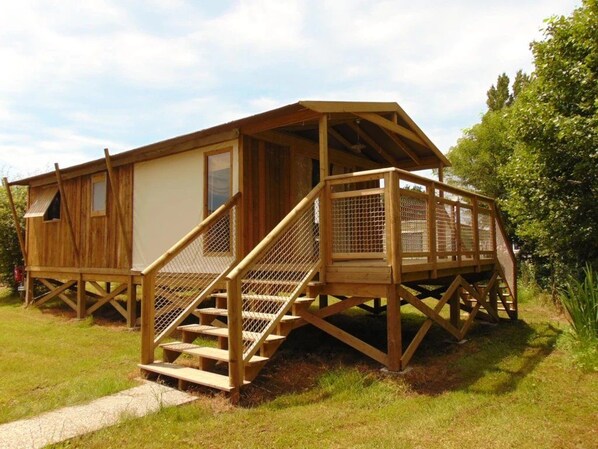 A wooden cabin with a covered porch and a staircase leading to a deck. - ZEcamping 3* piscine couverte animaux acceptés club enfant locatif TV (Avrillé)