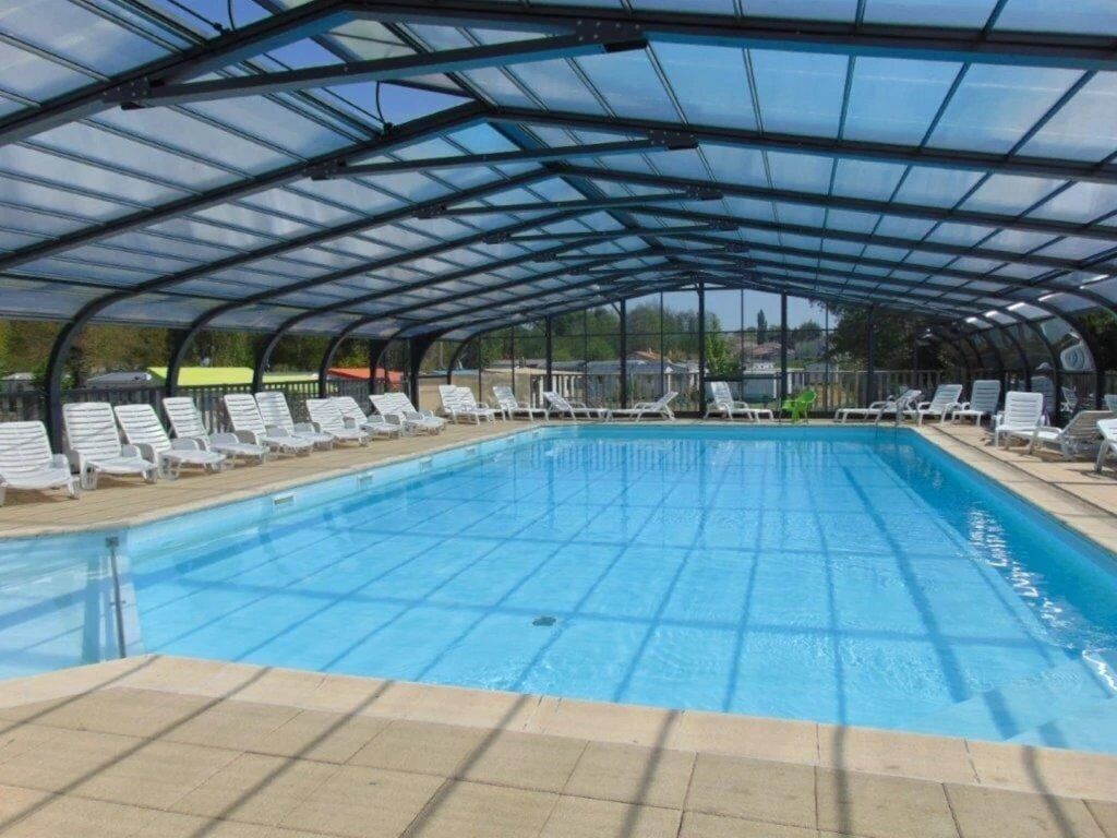 Une piscine couverte avec des chaises longues et un toit en verre.