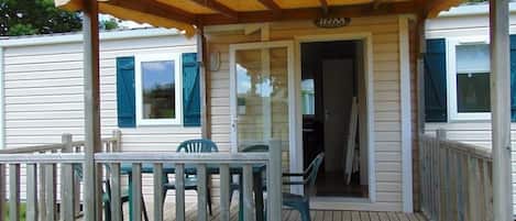 A covered porch with a wooden deck, a small table, and two chairs.