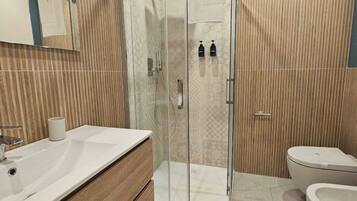 Een moderne badkamer met een glazen douchecabine, een houten wastafelmeubel, een toilet en een bidet.