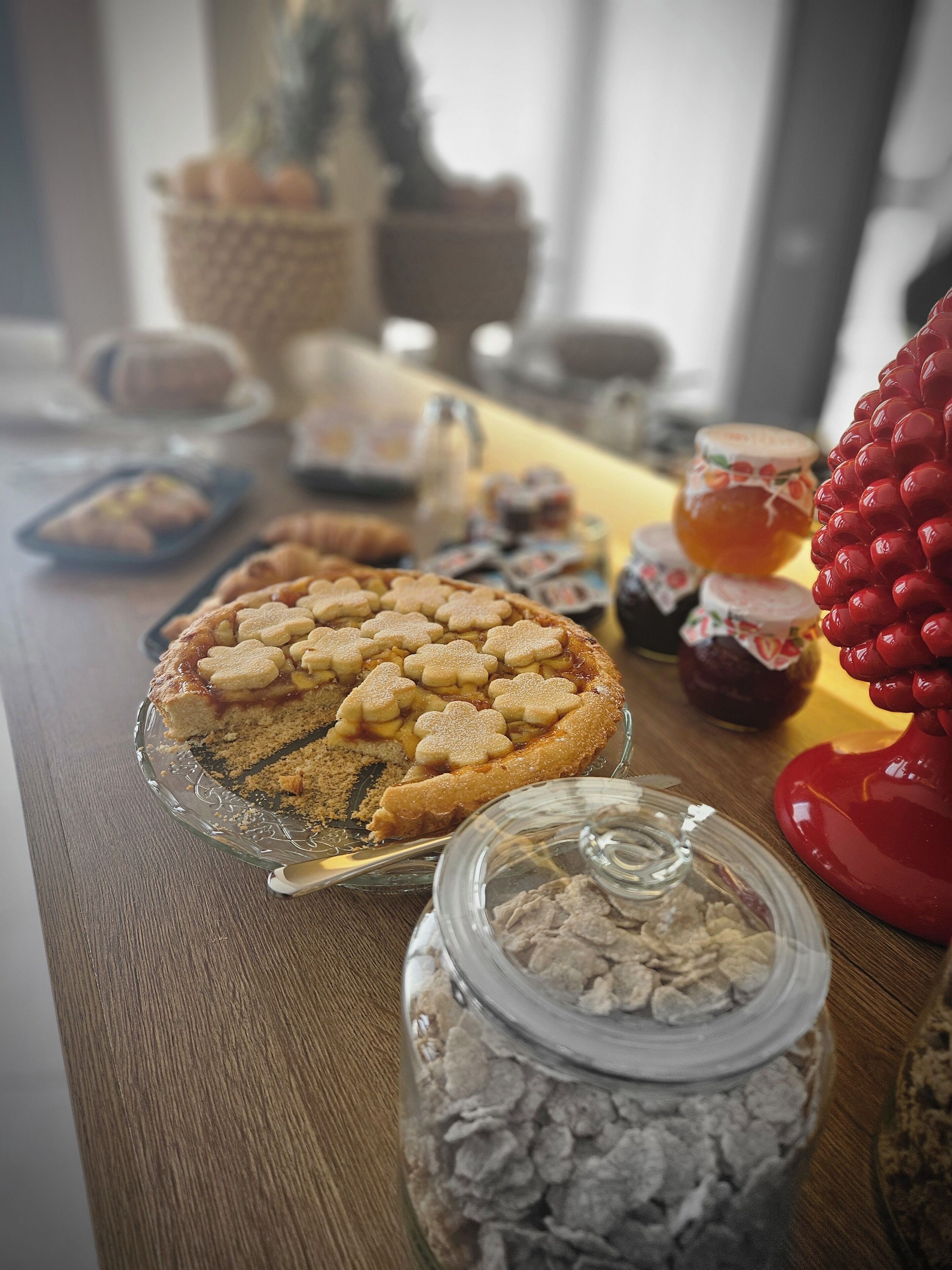 A table with a variety of food items including a pie, jars of preserves, and a decorative red object.