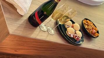 Et træbord med en champagneflaske, to glas, en tallerken med småkager, et stearinlys og et håndklæde.