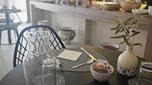 A dining area with a table set for two, featuring a vase with a plant, a bowl of fruit, and a glass of water. - Via del Mare Apulia B&B  Spa Suite (Rutigliano)