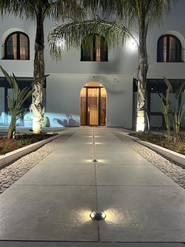 A building entrance with a central staircase, flanked by palm trees and illuminated by overhead lights. - Via del Mare Apulia B&B Spa Suite (Rutigliano)