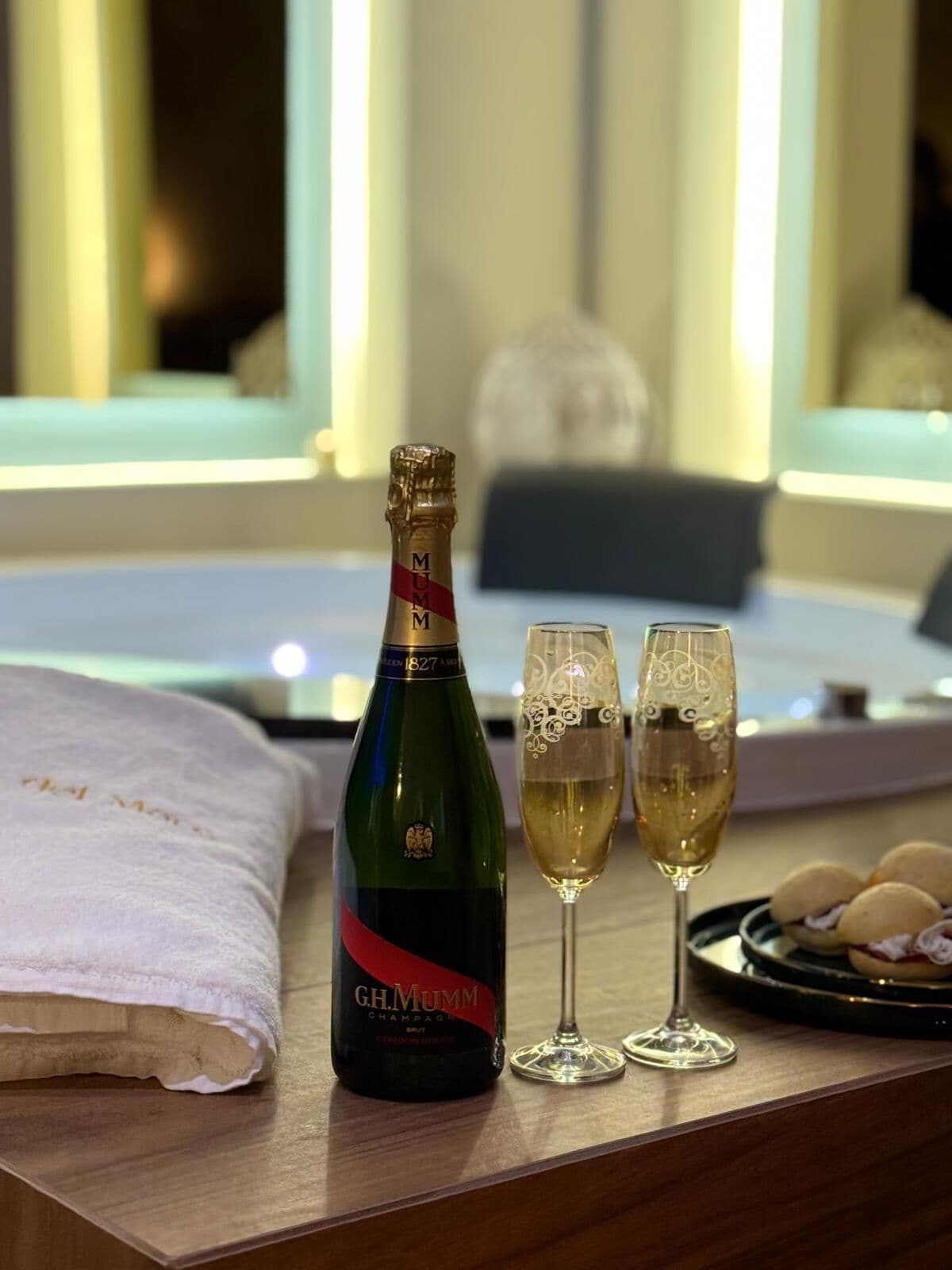 Una botella de champán, dos copas y un plato de galletas sobre una mesa de madera en una habitación de hotel.
