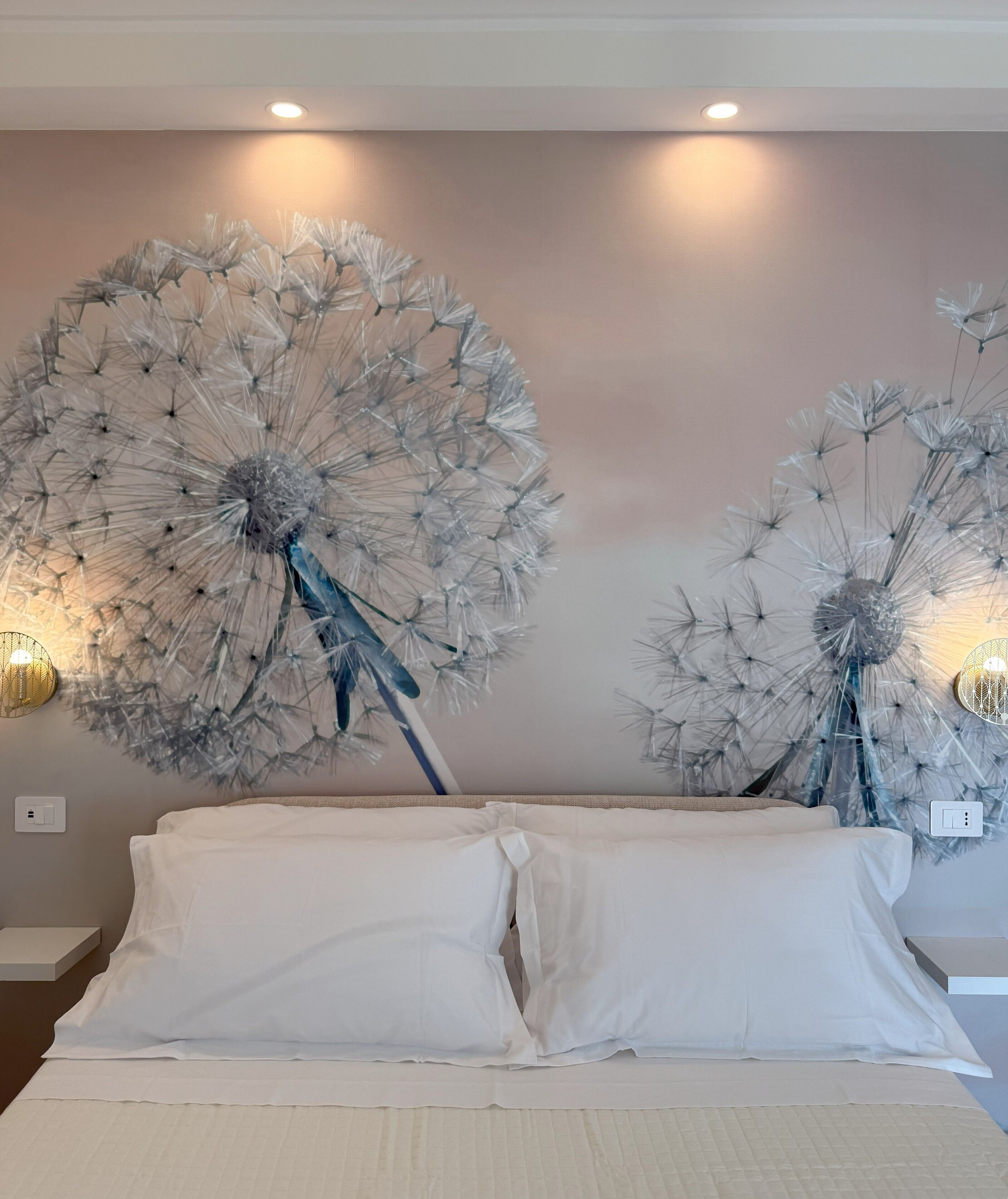 A bedroom with a large bed, white bedding, and two wall-mounted decorative dandelion sculptures.