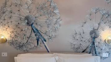 A bedroom with a large bed, white bedding, and two wall-mounted decorative dandelion sculptures.