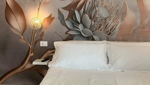 A hotel room with a bed, white linens, a decorative wall mural, and a bedside lamp. - Via del Mare Apulia B&B  Spa Suite (Rutigliano)