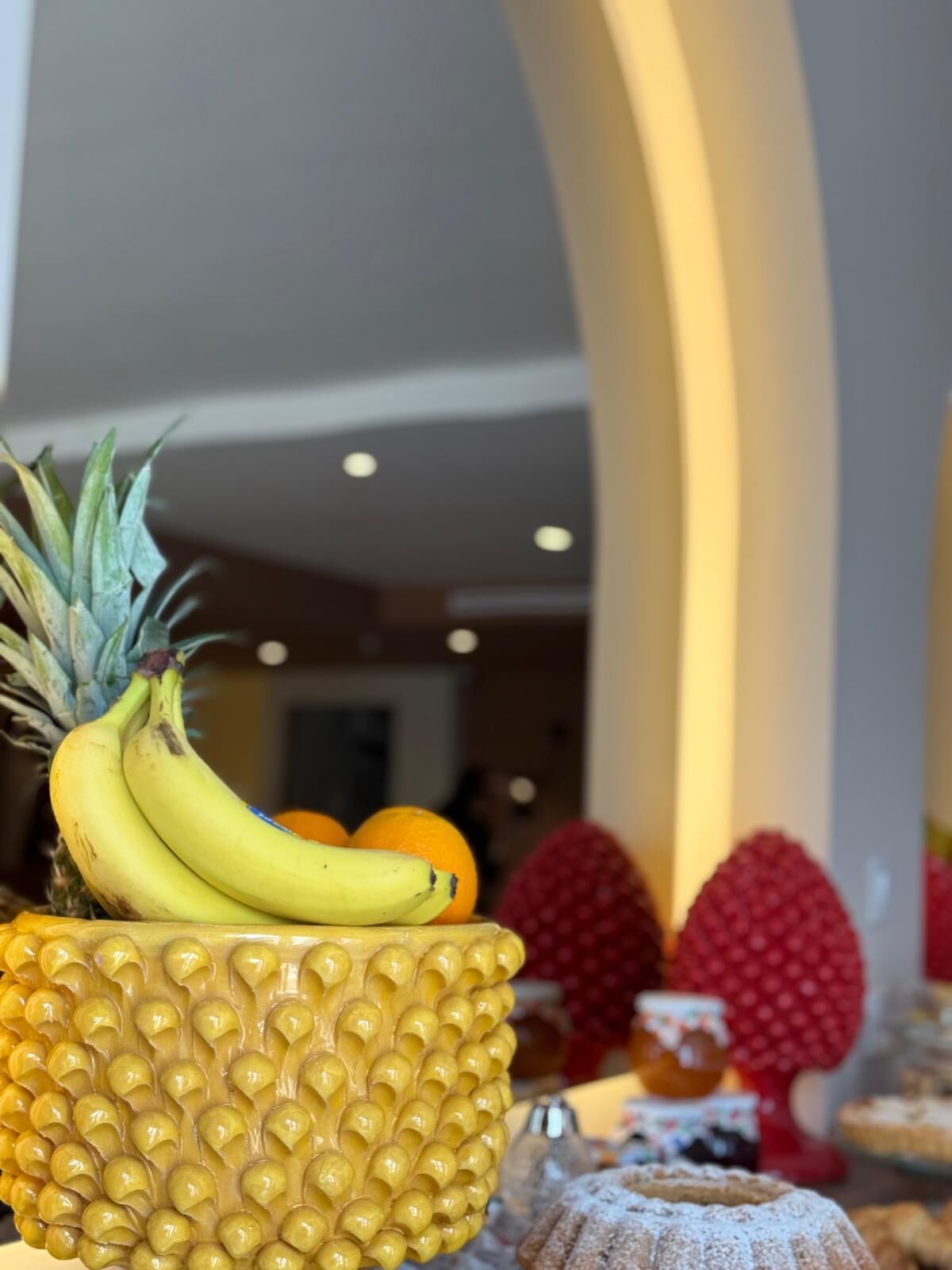 Una exposición de frutas con plátanos, naranjas y una piña en un cuenco texturizado.