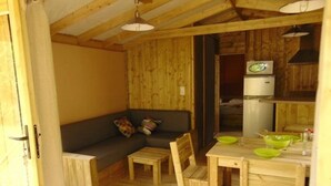 A cozy cabin interior with a wooden ceiling, a sofa, a dining table with chairs, and a kitchenette. - ZEcamping 3 étoiles piscine couverte locatif TV LV 43m2 (Avrillé)
