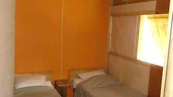 Een kleine, compacte kamer met twee eenpersoonsbedden, houten balken in het plafond en een raam met gordijnen.