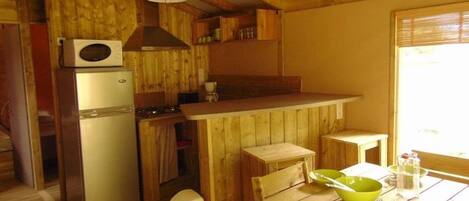 Una cocina compacta con armarios de madera, un refrigerador, una estufa y una mesa de comedor con boles verdes.