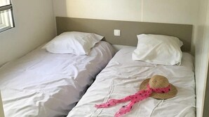 A twin room with two single beds, each with white bedding and pillows. There are two small wooden shelves above the beds. - ZEcamping 3* piscine couverte locatif TV LV 31m2 (Avrillé)