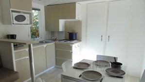 Une cuisine compacte équipée d’un four à micro-ondes, d’une cuisinière et d’un évier. On y trouve également une table à manger avec des assiettes et des verres.