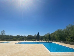 A rectangular swimming pool with a tiled deck, surrounded by lounge chairs and trees.