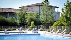 Piscina com espreguiçadeiras, cercada por uma grade e árvores.