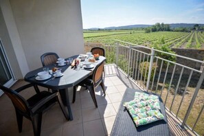 Un balcon avec une table dressée pour le petit-déjeuner, des chaises et une vue sur un vignoble.