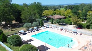 A swimming pool with lounge chairs and umbrellas, surrounded by trees and a hilly landscape. - ZEcamping 3* dog friendly piscine dans le parc régional du Verdon (Valensole)