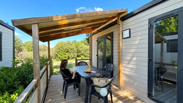 A covered outdoor seating area with a table and chairs, a wooden pergola, and a sliding glass door leading to a deck. - ZEcamping 3* dog friendly piscine dans le parc régional du Verdon (Valensole)