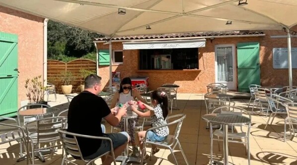 An outdoor patio area with metal chairs and tables, a covered seating area, and a building with a tiled roof and a window displaying a menu.