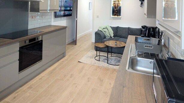 A modern kitchen with a built-in oven, a dining area with a sofa and coffee table, and a large window providing natural light. - Prime Location 5 Bed En-suite 6 Bathrooms in Derby Sleeps up to 10 People. (Derby)