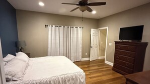 Un dormitorio con cama, piso de madera, ventilador de techo, cómoda y televisor.