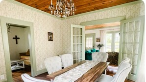 A dining area with a wooden table, white upholstered chairs, and a chandelier.