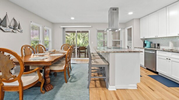 A modern kitchen with white cabinets, a central island, and a dining area with wooden chairs and a table. - Frippin Graytful, Golf Cart Included, Pet Friendly - 120 Sea Otter (Fripp Island)