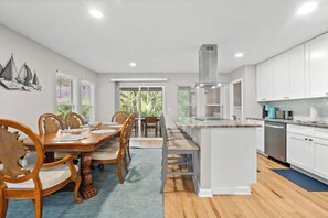 Een moderne keuken met witte kastjes, een centraal eiland en een eethoek met houten stoelen en een tafel.