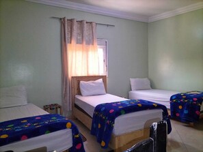 Una habitación con tres camas, cada una con una colcha azul de lunares, cabeceros de madera y ropa de cama blanca.