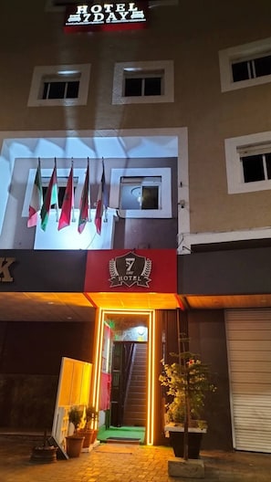 A hotel entrance with a sign reading '7 DAY HOTEL,' a set of flags, and a staircase leading to the entrance. - HOTEL 7DAYS (Dakhla)