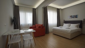 Et moderne hotelværelse med en seng, en rød sofa, et spisebord med stole og et fjernsyn.