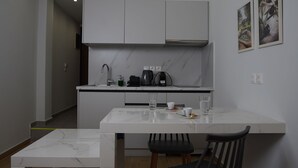 Et moderne køkken med hvide skabe, en marmor bordplade og en indbygget ovn. Der er et spisebord med stole og en loftslampe.