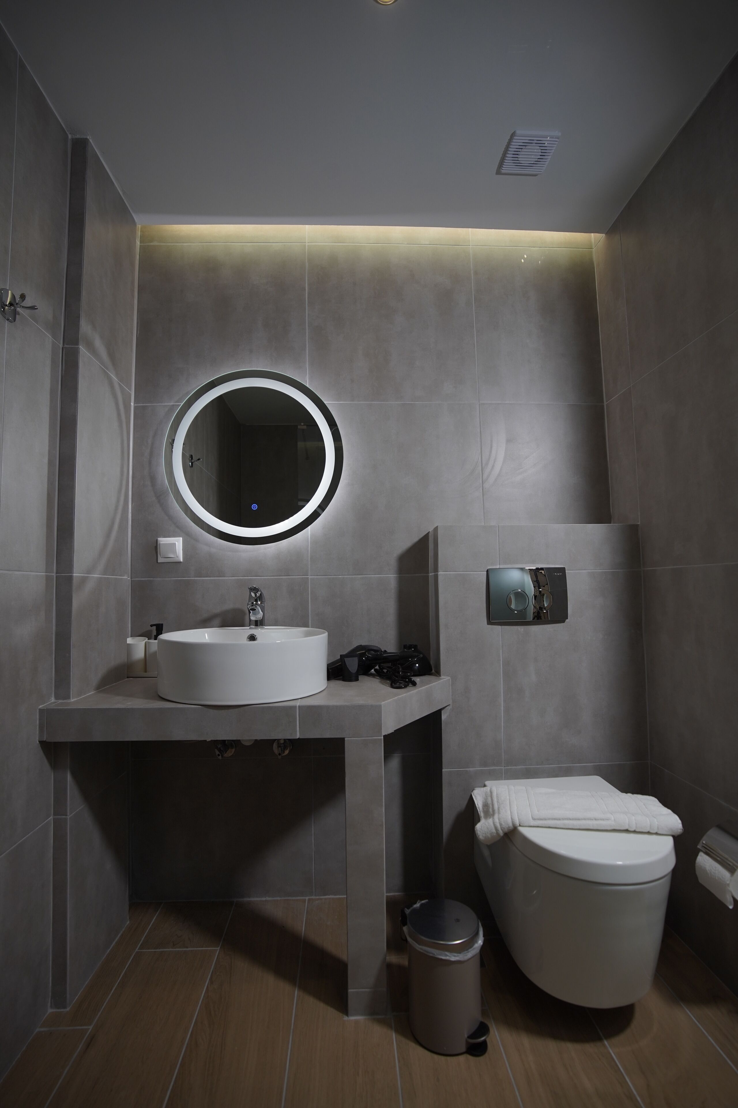 Ein modernes Badezimmer mit rundem Spiegel, Waschbecken, Toilette und Mülleimer.