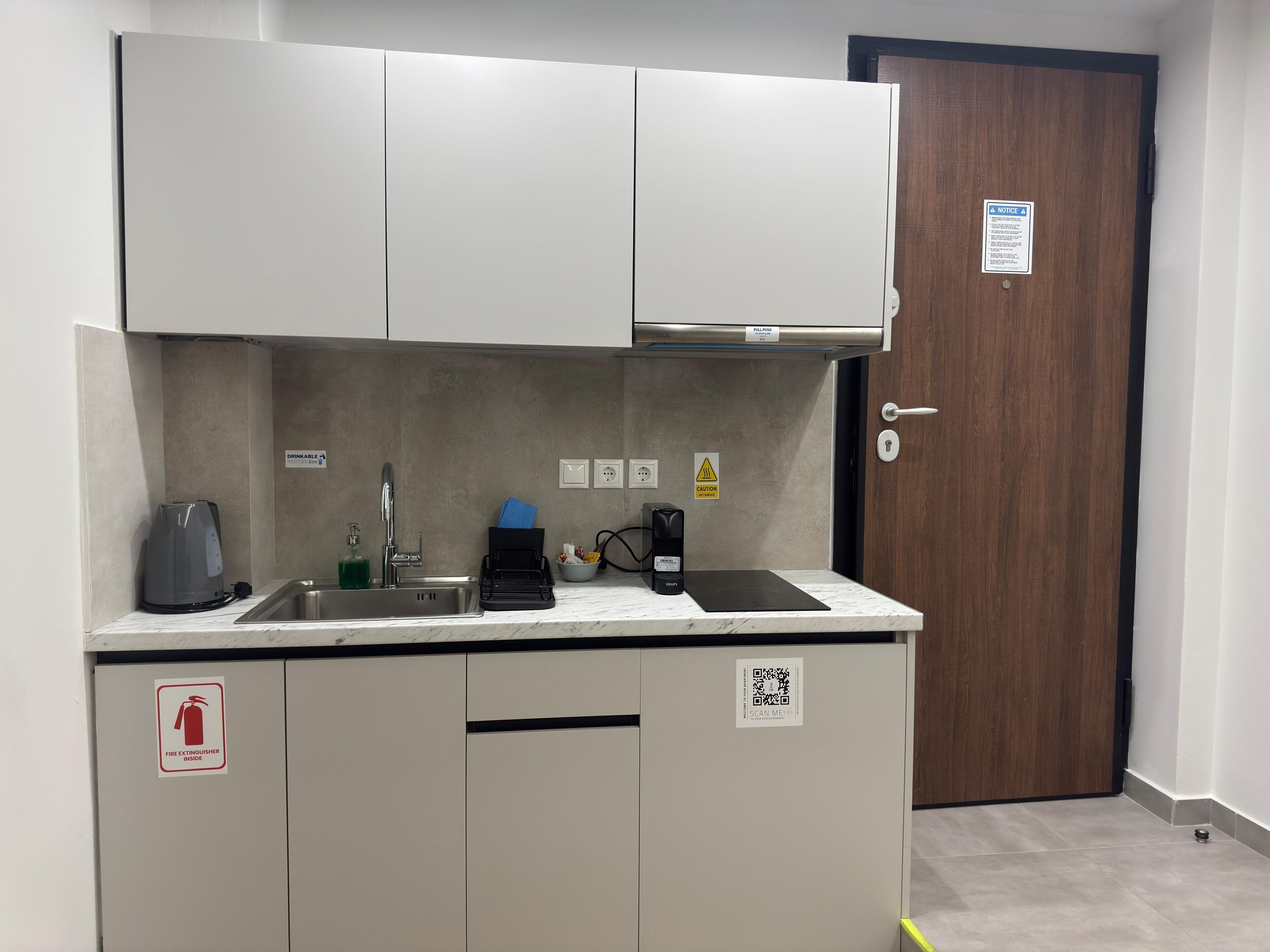 Una kitchenette compacta con un lavamanos, una cafetera, un hervidor y una pequeña encimera.