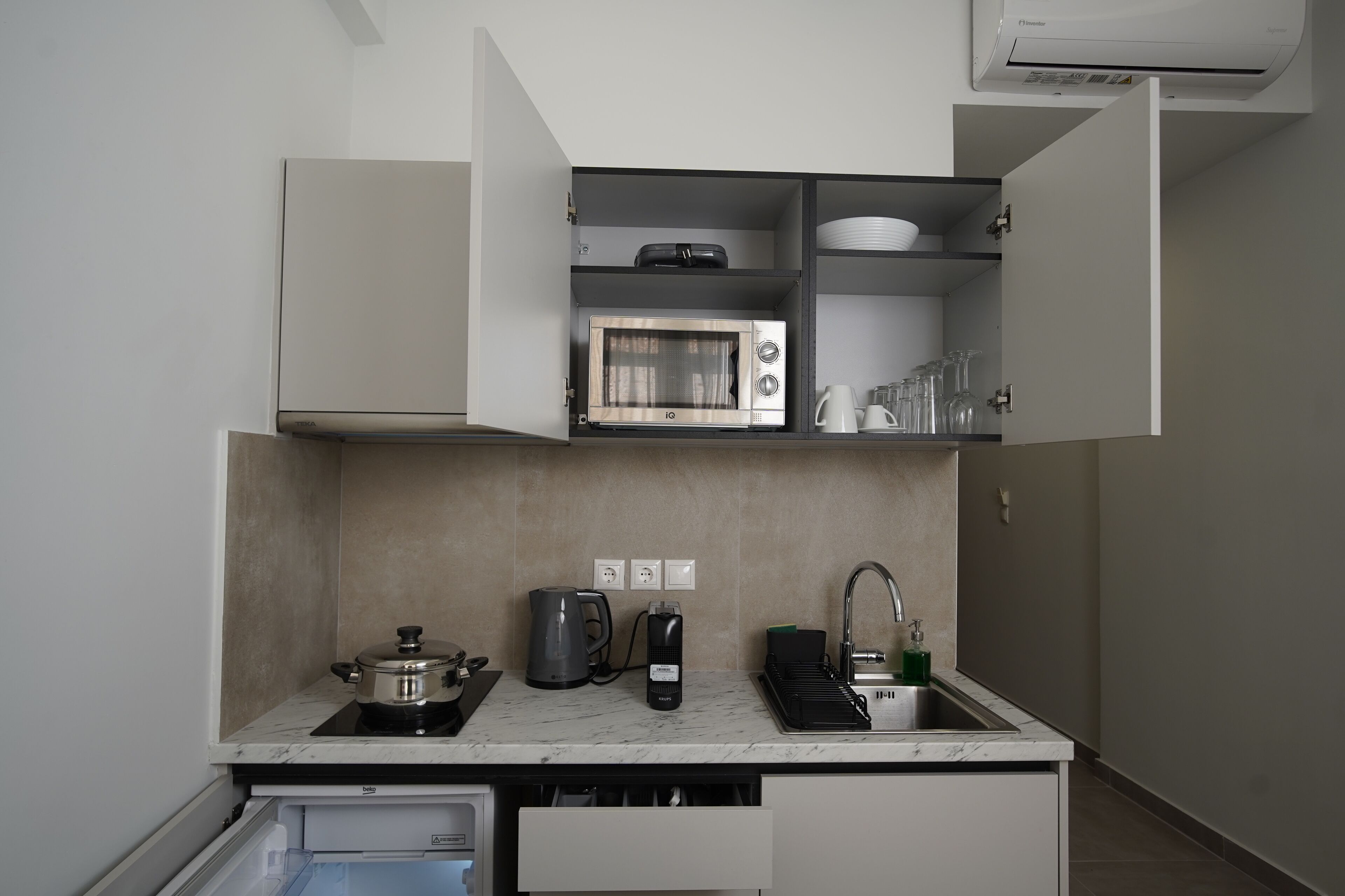 A compact kitchen with a microwave, kettle, and coffee maker on the countertop.