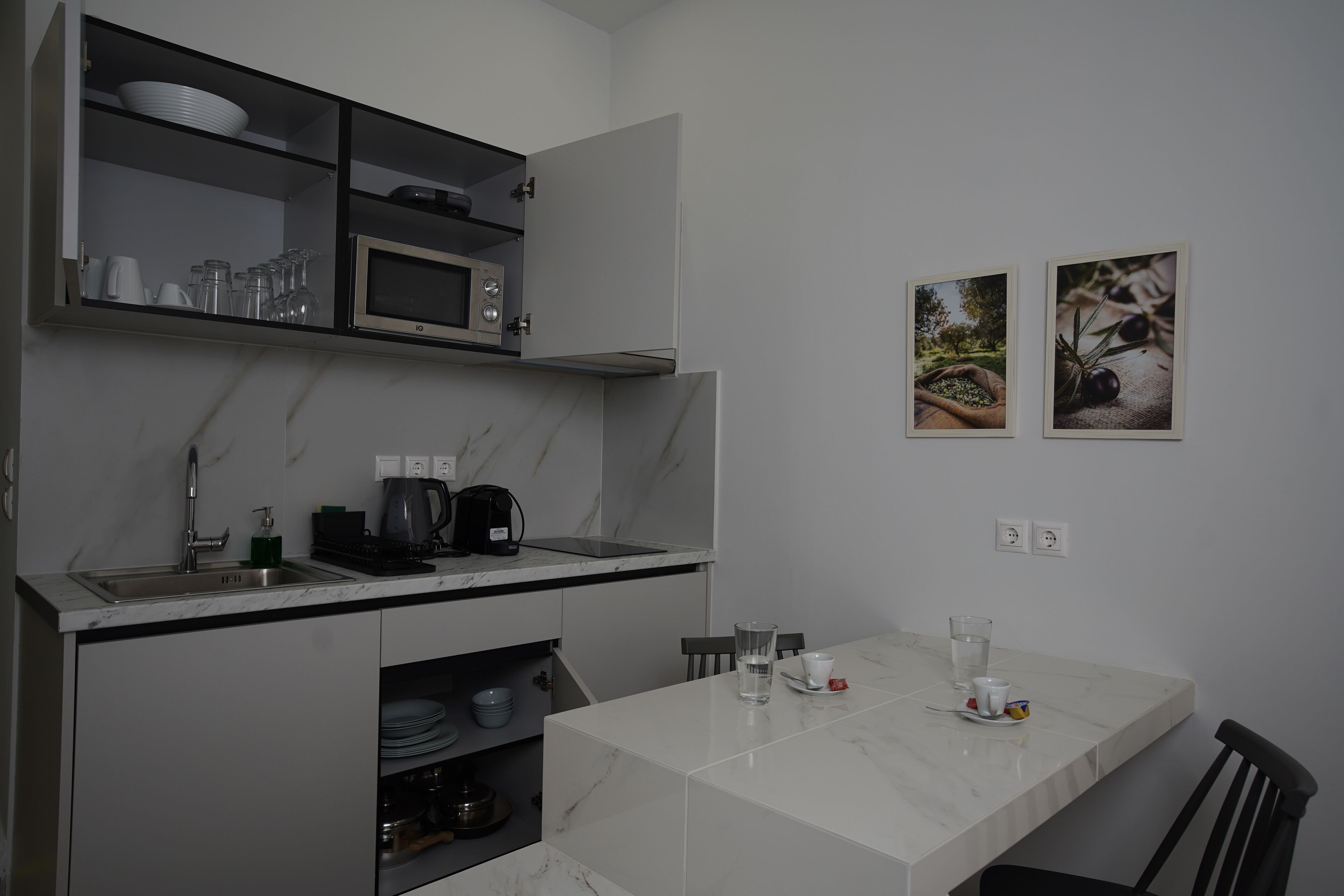 Una cocina moderna con microondas integrado, cafetera y un lavabo. Hay una mesa de comedor con sillas y un mueble pequeño debajo de la encimera.